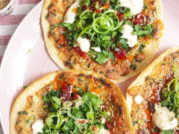 Three prawn toast tacos topped with herbs and aioli on a pink plate.