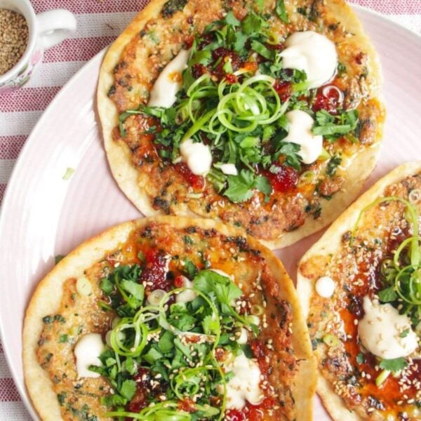 Three prawn toast tacos topped with herbs and aioli on a pink plate.