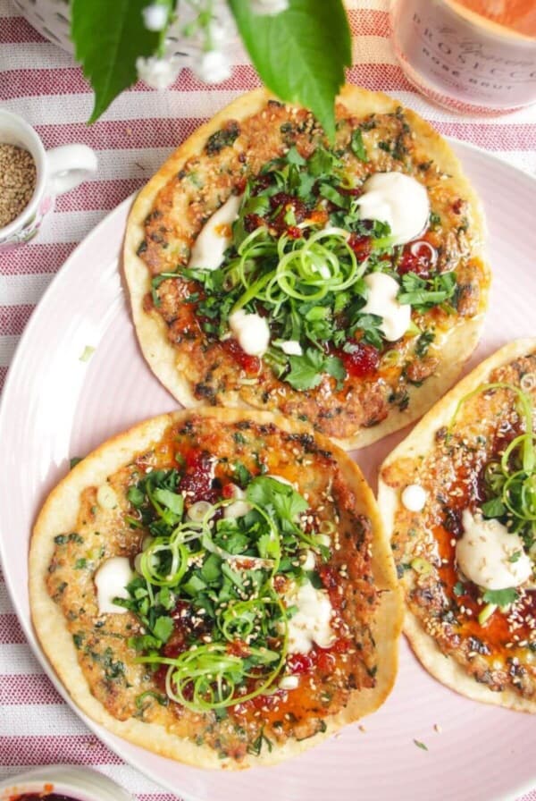 Three prawn toast tacos topped with herbs and aioli on a pink plate.