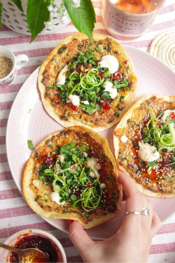 Three prawn toast tacos topped with herbs and aioli on a pink plate.