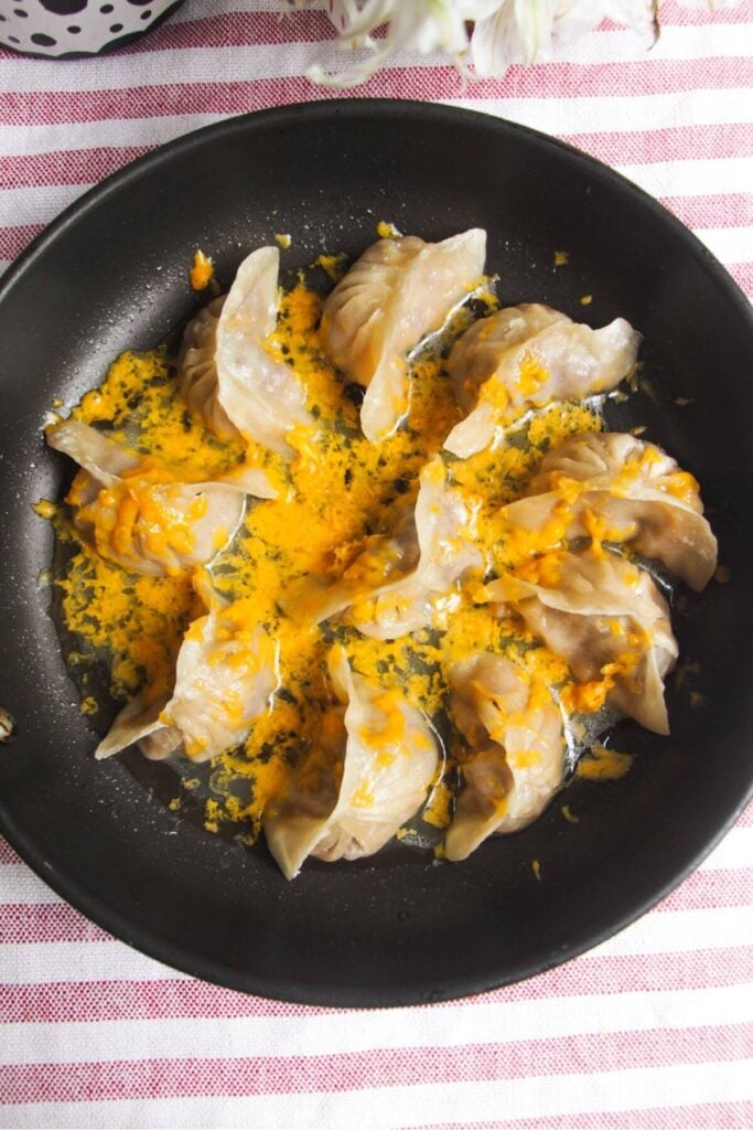 Grated cheese on top of cheeseburger dumplings in a small pan.