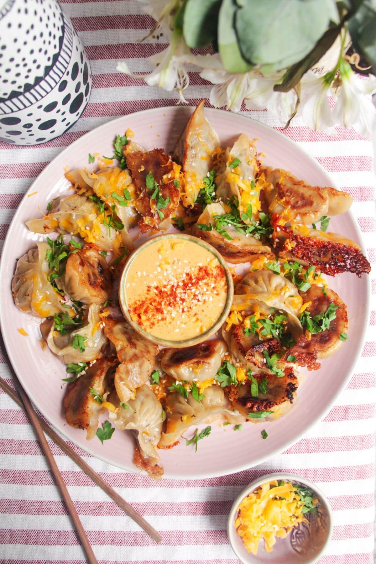 Crispy cheeseburger dumplings on a pink plate with small bowl of burger sauce in the middle.