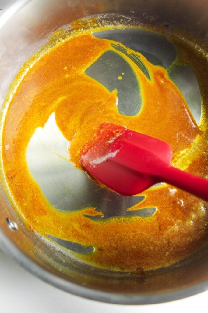 Red spatula stirring spices in a large pan.