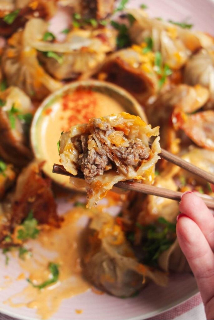 Hand holding chopstick holding up an open cheeseburger dumpling.