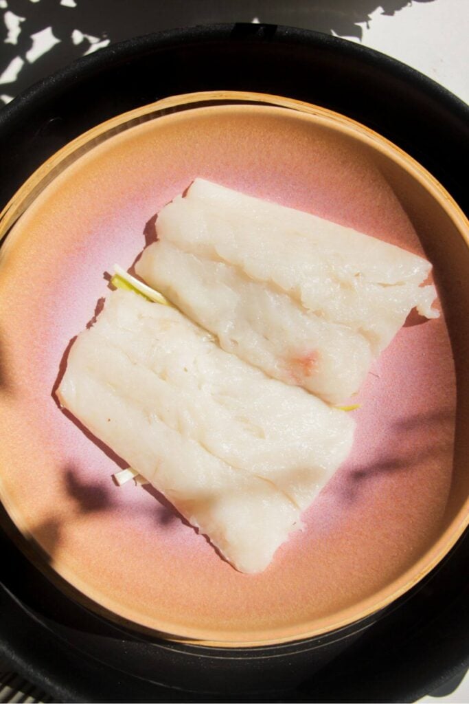 Two fish fillets in a pink bowl in a steamer basket.