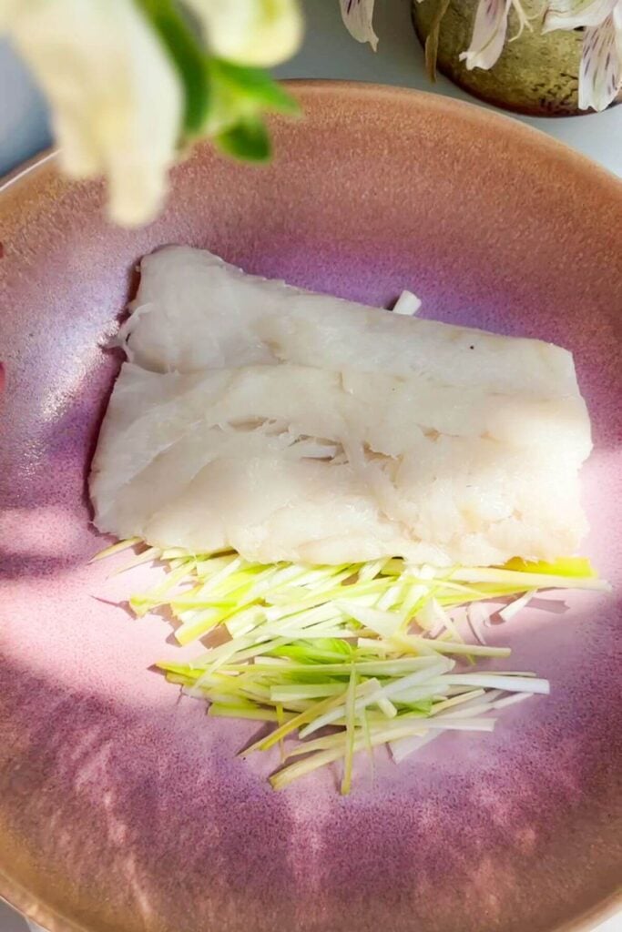 One piece of fish on top of sliced scallions in a pink bowl.