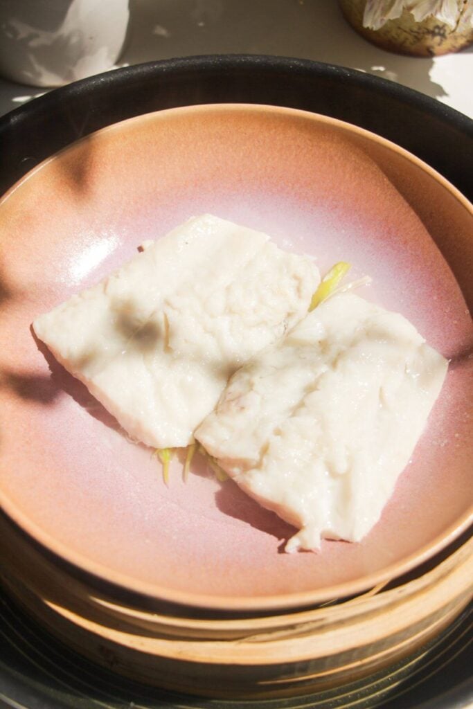 Two steamed fish fillets in a pink bowl in a steamer basket.
