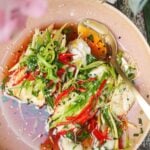 Two fish fillets topped with scallions, ginger and chili in a pink bowl.