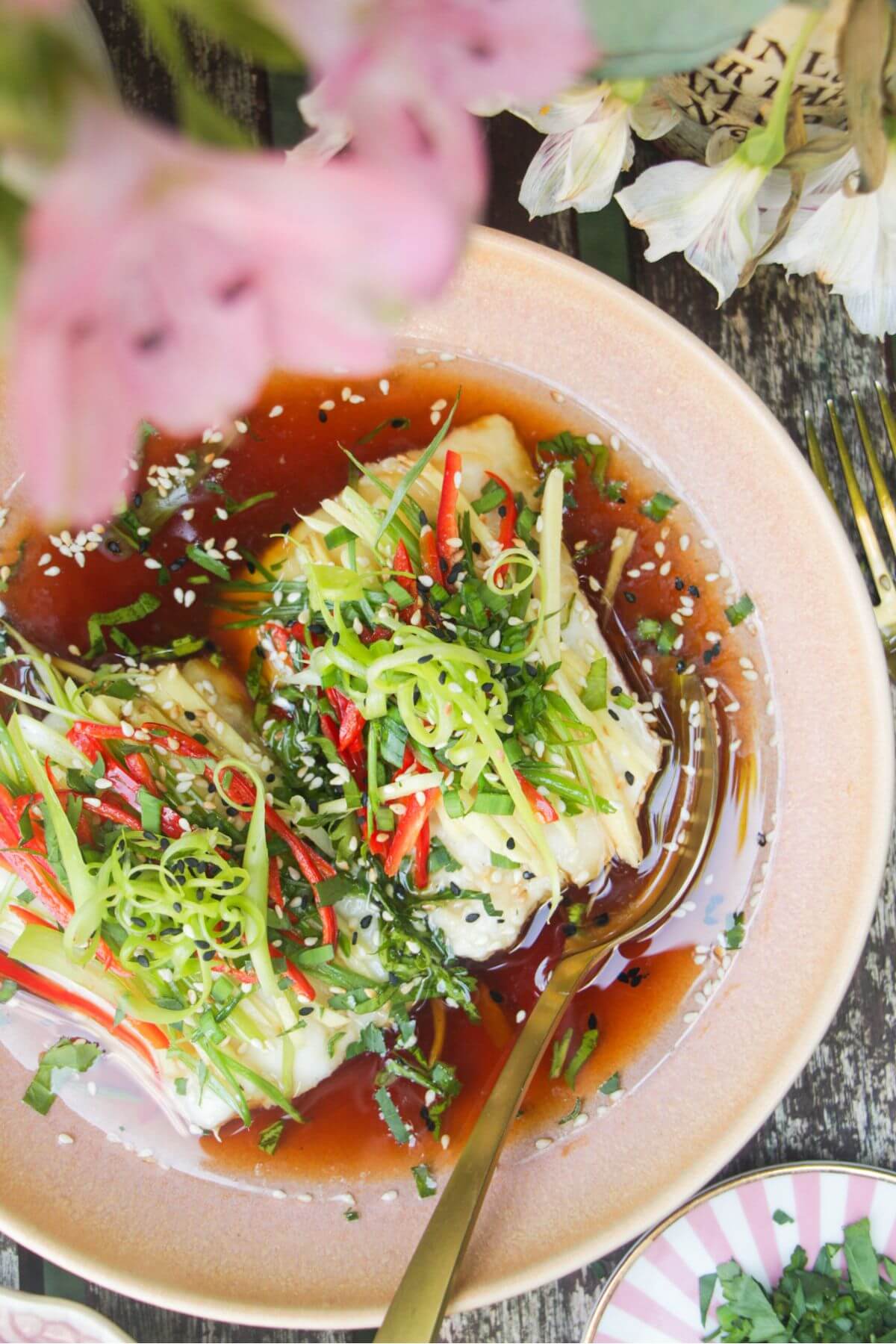 Two fish fillets topped with scallions, ginger and chili in a pink bowl.