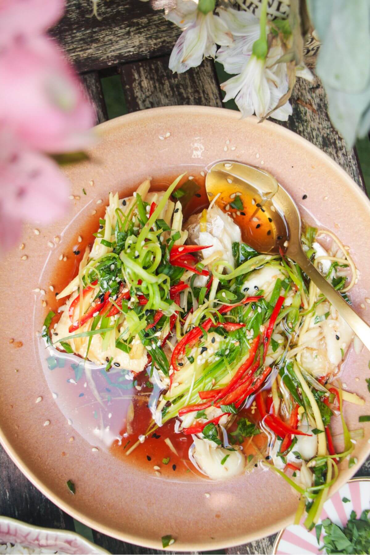 Two fish fillets topped with scallions, ginger and chili in a pink bowl.