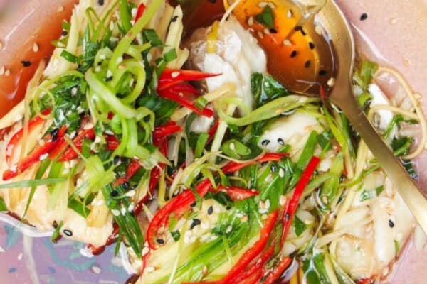 Two fish fillets topped with scallions, ginger and chili in a pink bowl.