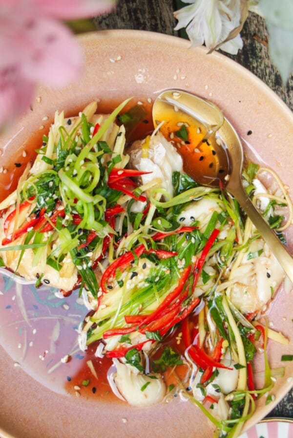 Two fish fillets topped with scallions, ginger and chili in a pink bowl.