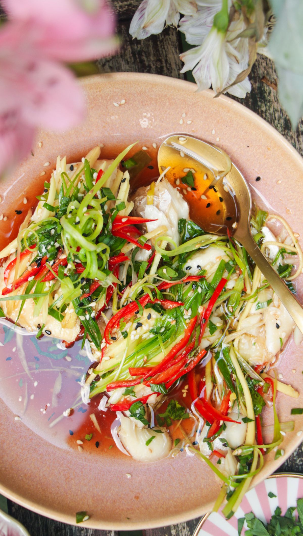 Two fish fillets topped with scallions, ginger and chili in a pink bowl.