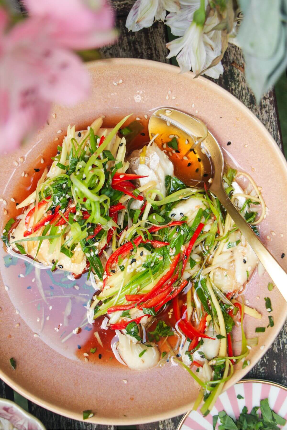 Two fish fillets topped with scallions, ginger and chili in a pink bowl.