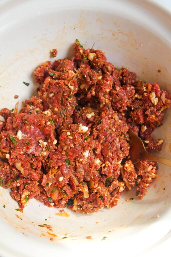 Ground beef mixed with spices, herbs and feta in a mixing bowl.