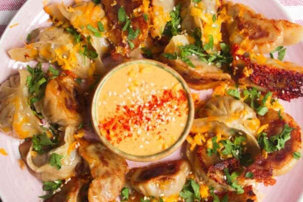 Crispy cheeseburger dumplings on a pink plate with small bowl of burger sauce in the middle.