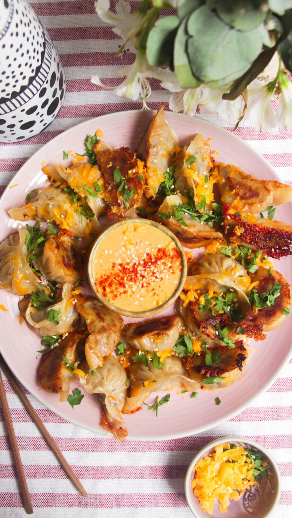 Crispy cheeseburger dumplings on a pink plate with small bowl of burger sauce in the middle.