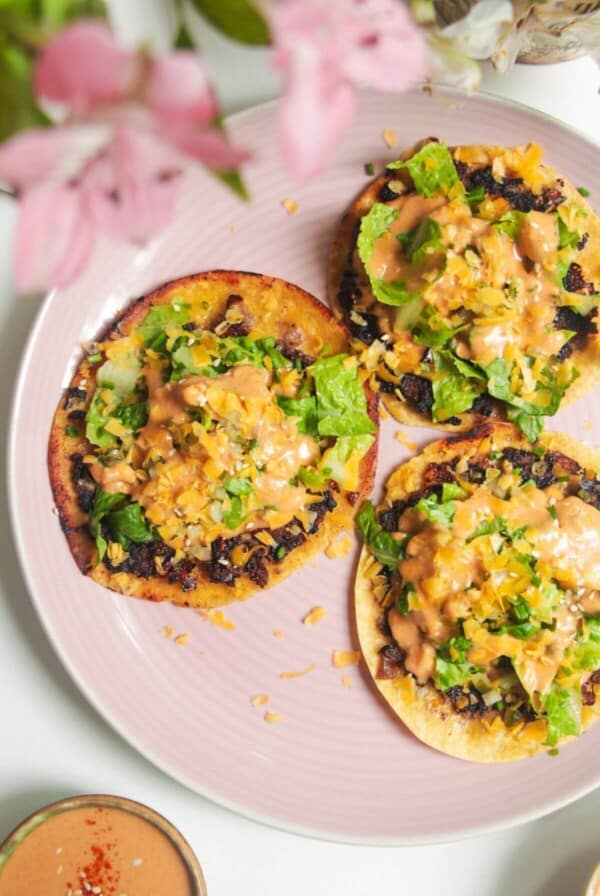 Three smash cheeseburger tacos on a pink plate.