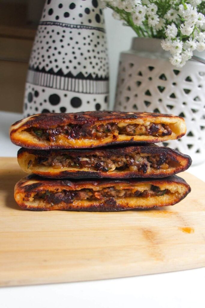 Three cooked stuffed flatbreads on top of each other on a wooden board.