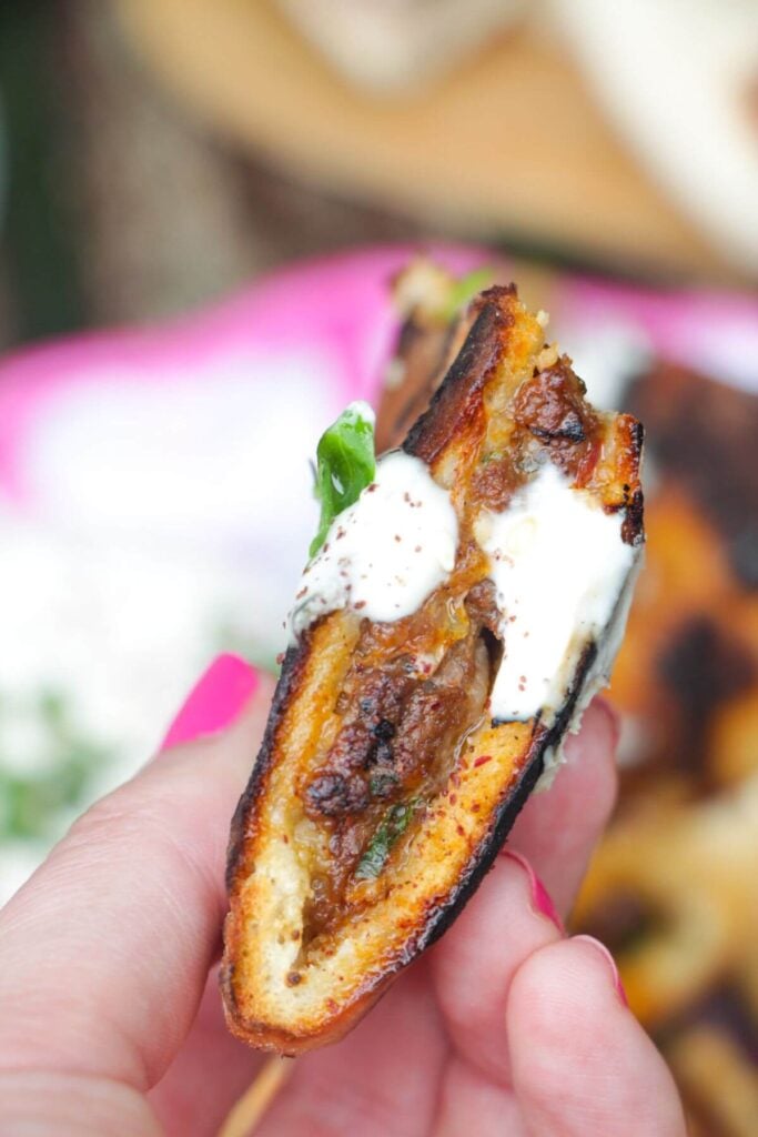 Hand holding up a piece of stuffed flatbread dipping in tahini sauce.