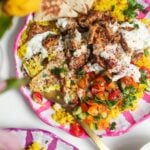 Chicken, salad and rice on a pink and white striped plate with pita bread on the side.