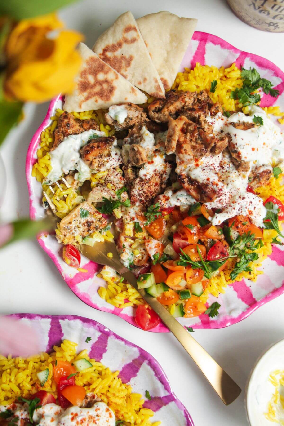 Chicken, salad and rice on a pink and white striped plate with pita bread on the side.