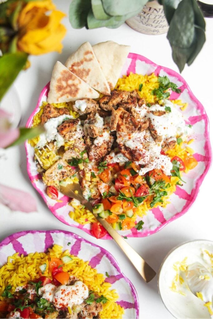 Chicken, salad and rice on a pink and white striped plate with pita bread on the side.