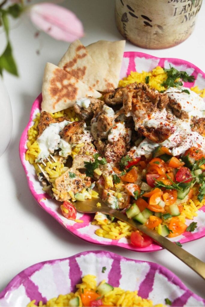 Chicken, salad and rice on a pink and white striped plate with pita bread on the side.