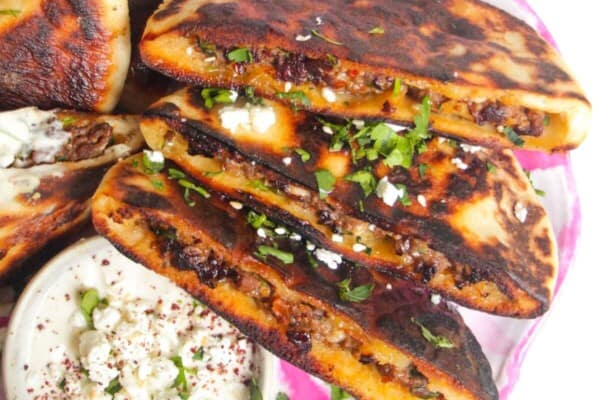 Three stuffed flatbreads on a pink and white plate with tahini sauce on the side.