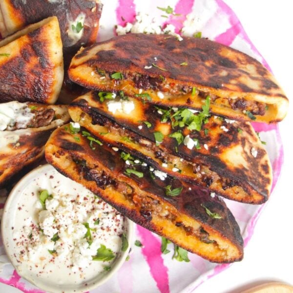Three stuffed flatbreads on a pink and white plate with tahini sauce on the side.