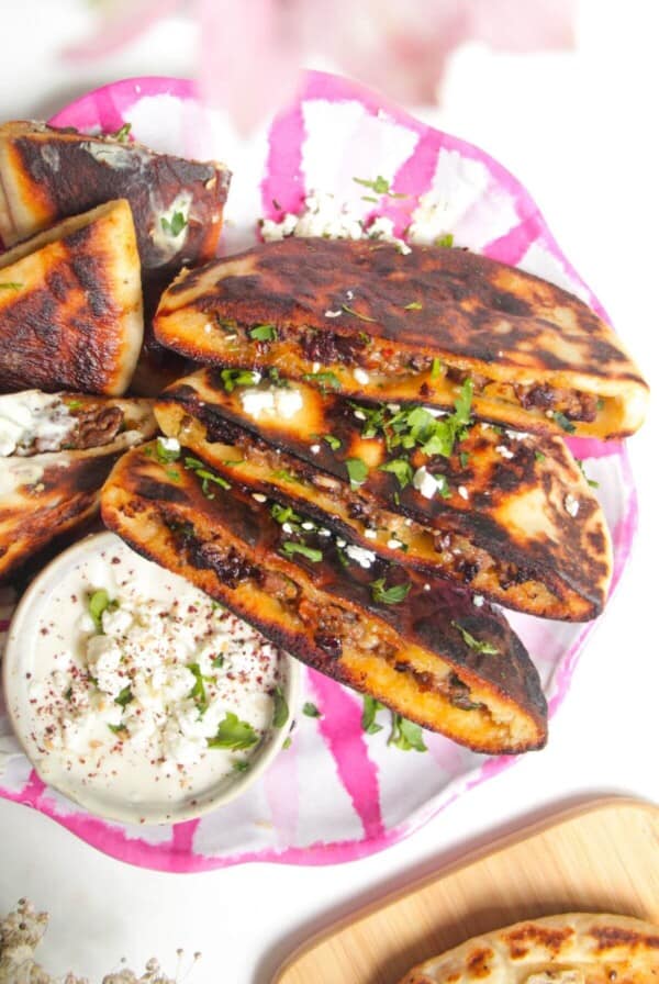 Three stuffed flatbreads on a pink and white plate with tahini sauce on the side.