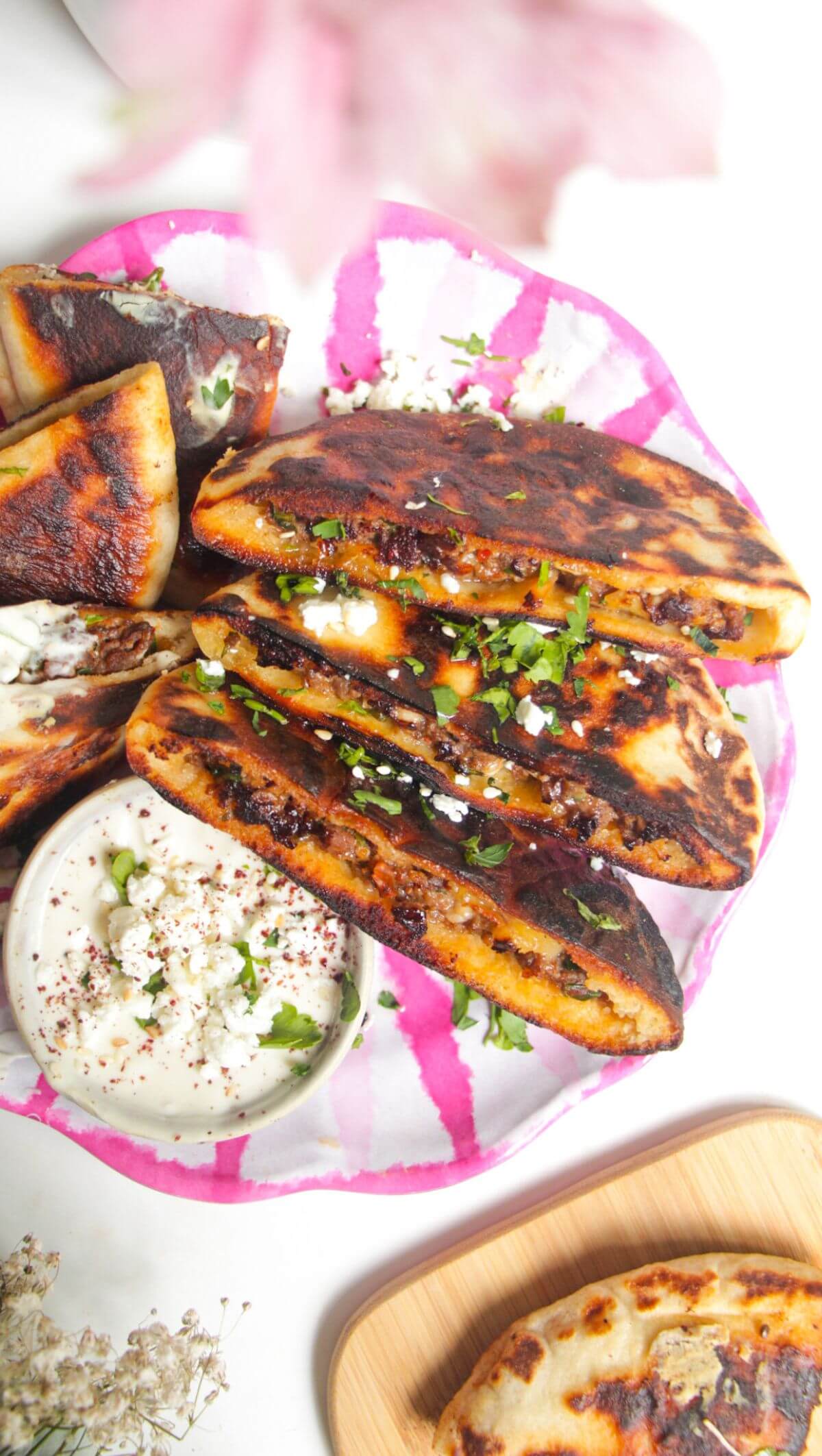 Three stuffed flatbreads on a pink and white plate with tahini sauce on the side.