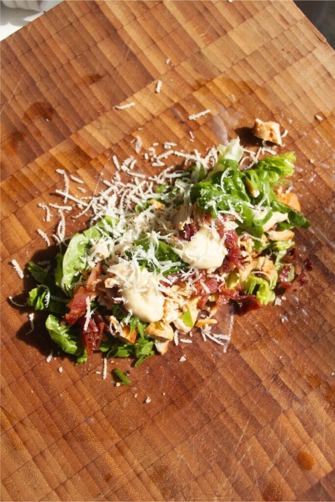 Lettuce, chicken, bacon, parmesan and dressing on top of rice paper on a wooden board.