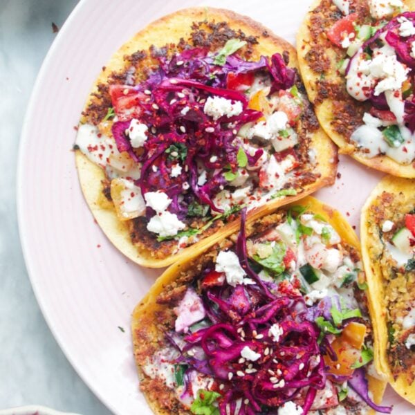 Four smash falafel tacos on a pink plate with salad on the side.