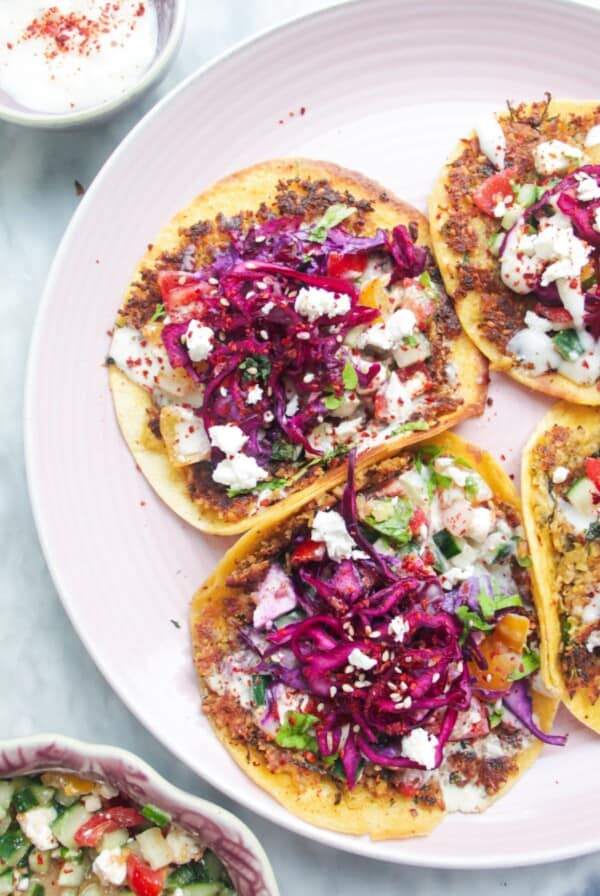 Four smash falafel tacos on a pink plate with salad on the side.