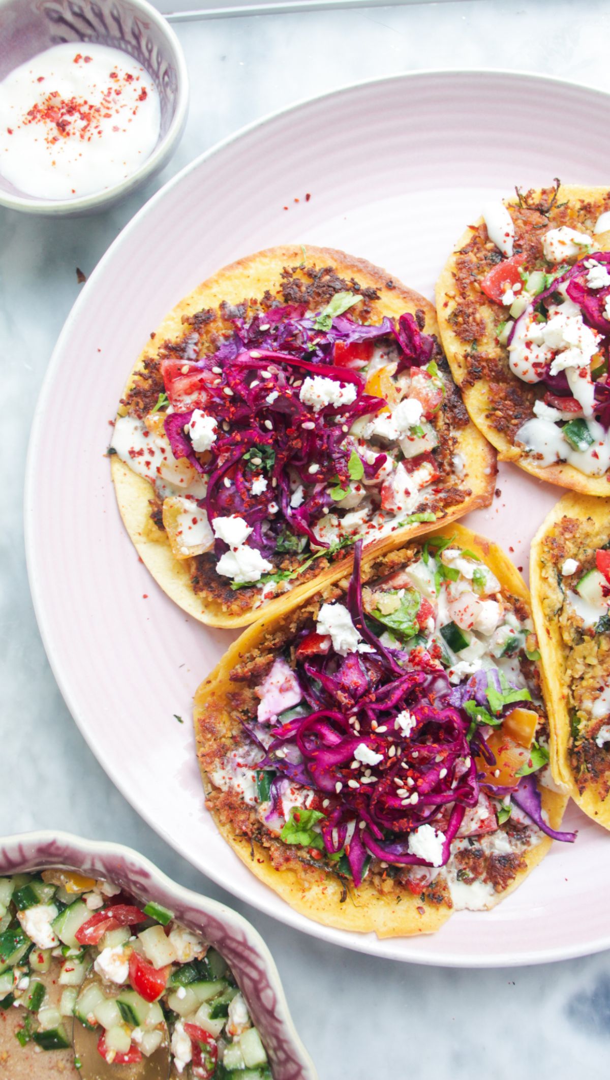 Four smash falafel tacos on a pink plate with salad on the side.