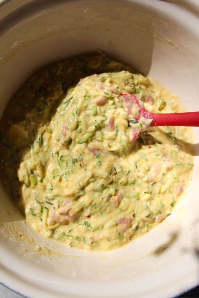Spatula mixing batter with zucchini bread in a large bowl.