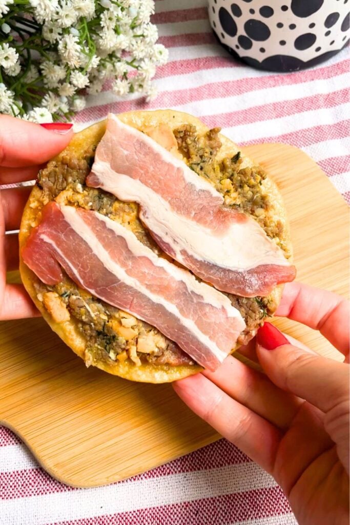 Bacon on top of cheeseburger mix on a taco.