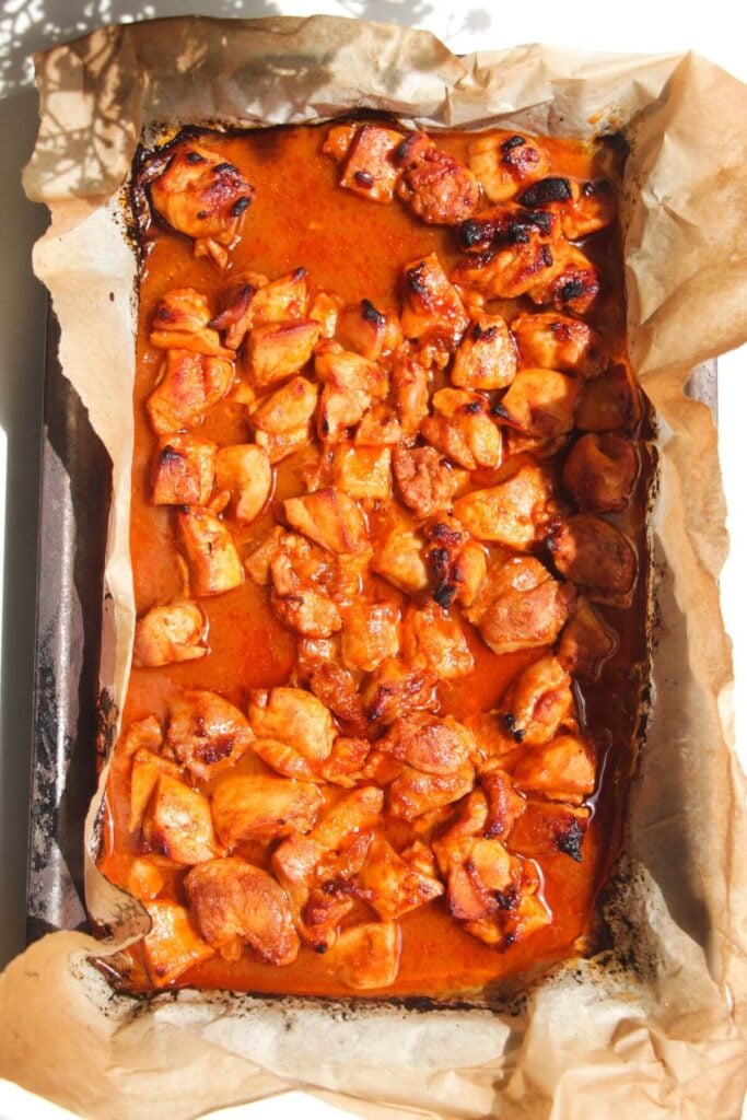 Cooked Buffalo chicken pieces on a lined oven tray.