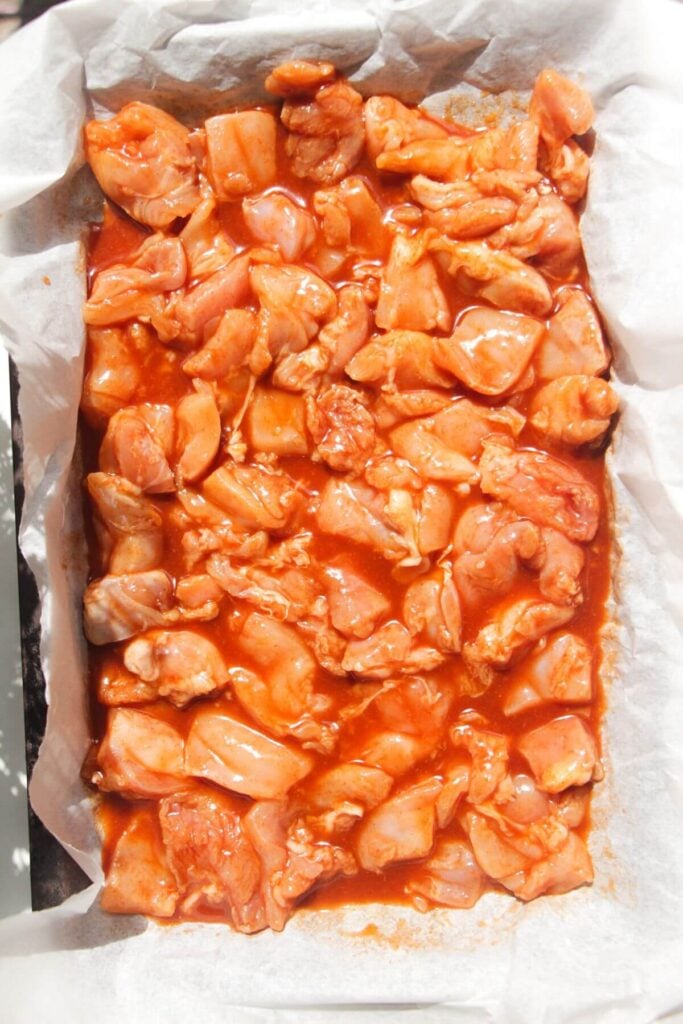 Buffalo marinated chicken thigh pieces on a lined oven tray.