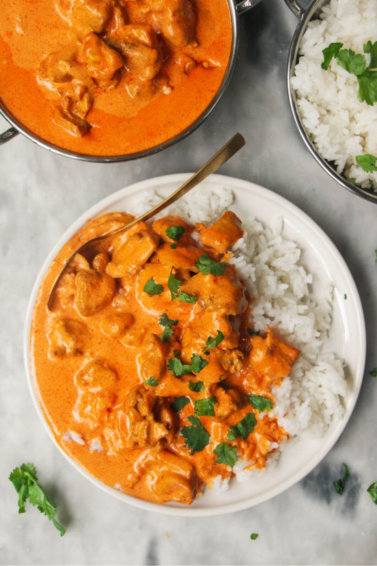 White plate with rice and butter chicken with bowl of butter chicken in the background and garlic naan.