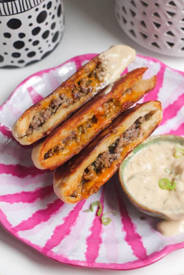 Three cheeseburger flatbreads on a pink and whiteplate with burger sauce on the side.