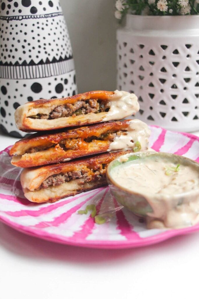Three cheeseburger flatbreads on a pink and whiteplate with burger sauce on the side.
