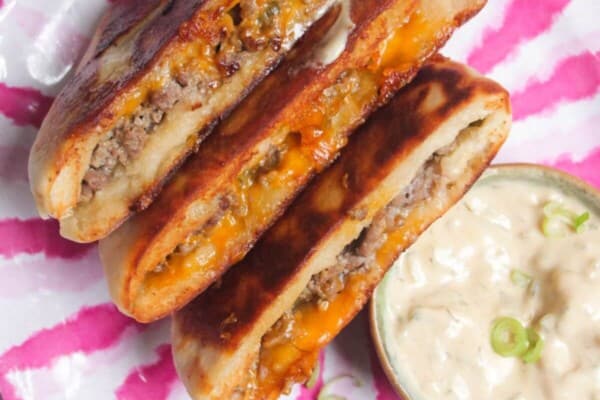 Three cheeseburger flatbreads on a pink and whiteplate with burger sauce on the side.