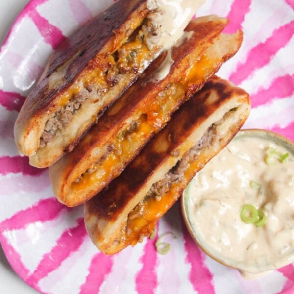 Three cheeseburger flatbreads on a pink and whiteplate with burger sauce on the side.