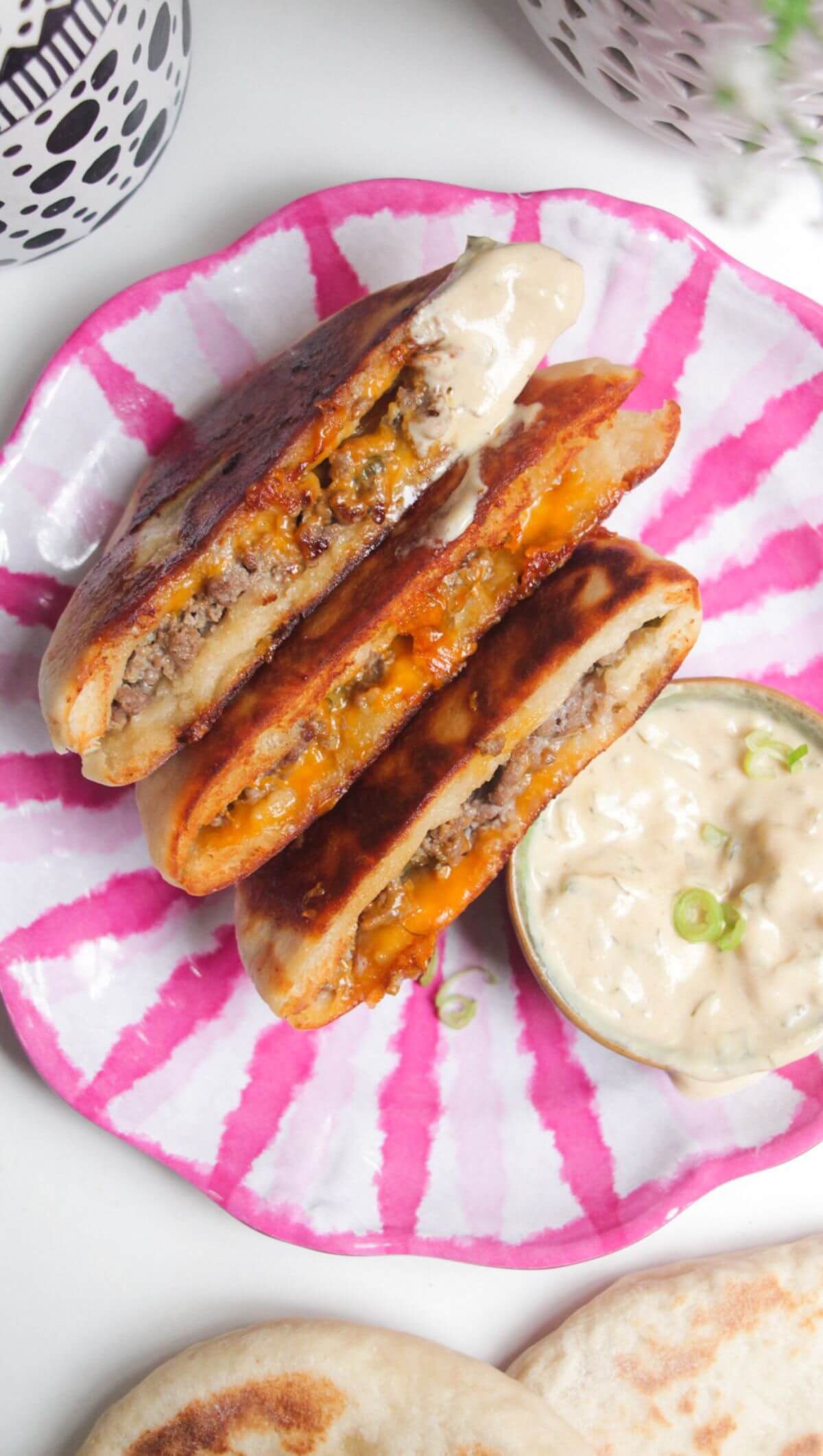 Three cheeseburger flatbreads on a pink and whiteplate with burger sauce on the side.