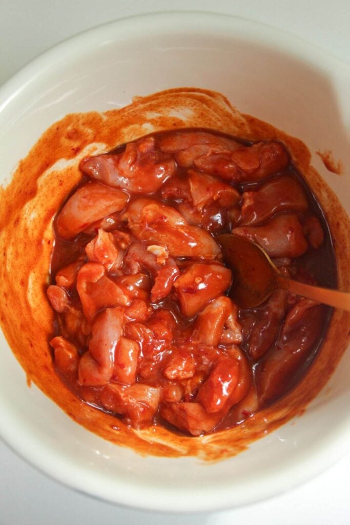 Mixing Buffalo marinade with chicken thigh pieces.