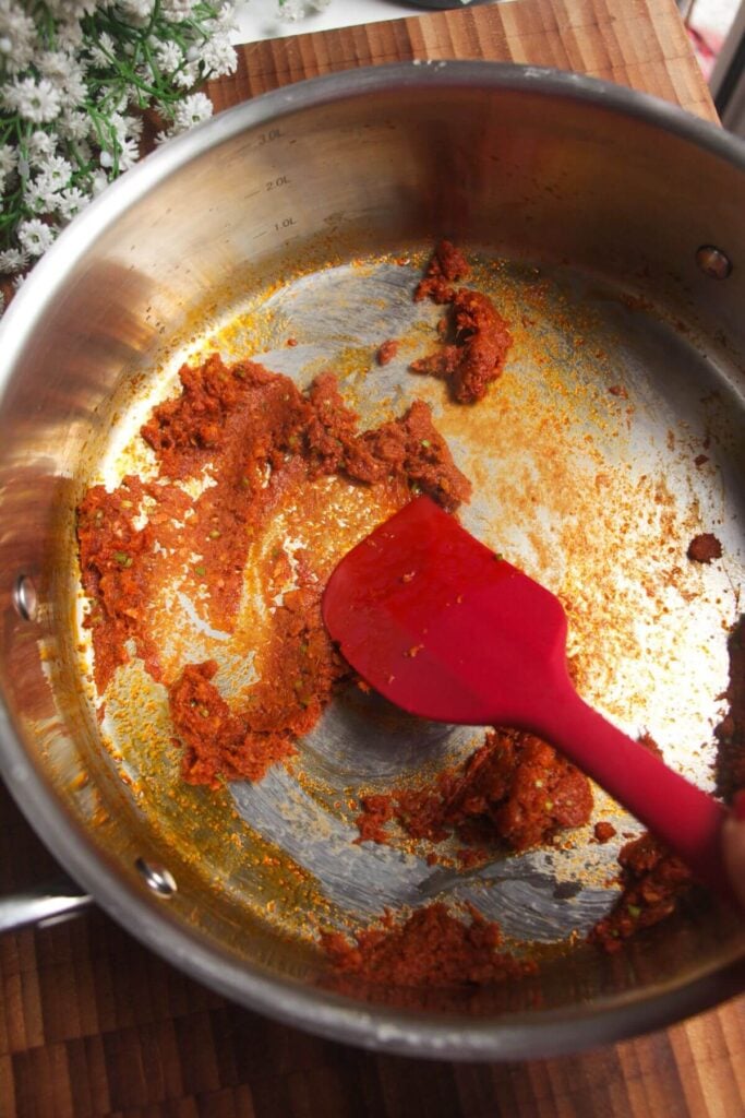 Red curry paste being stirred in a large pan.