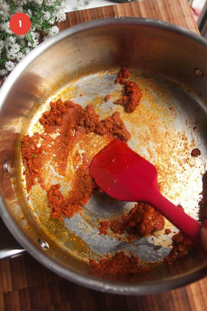 Spatula stirring red curry paste in a pan.