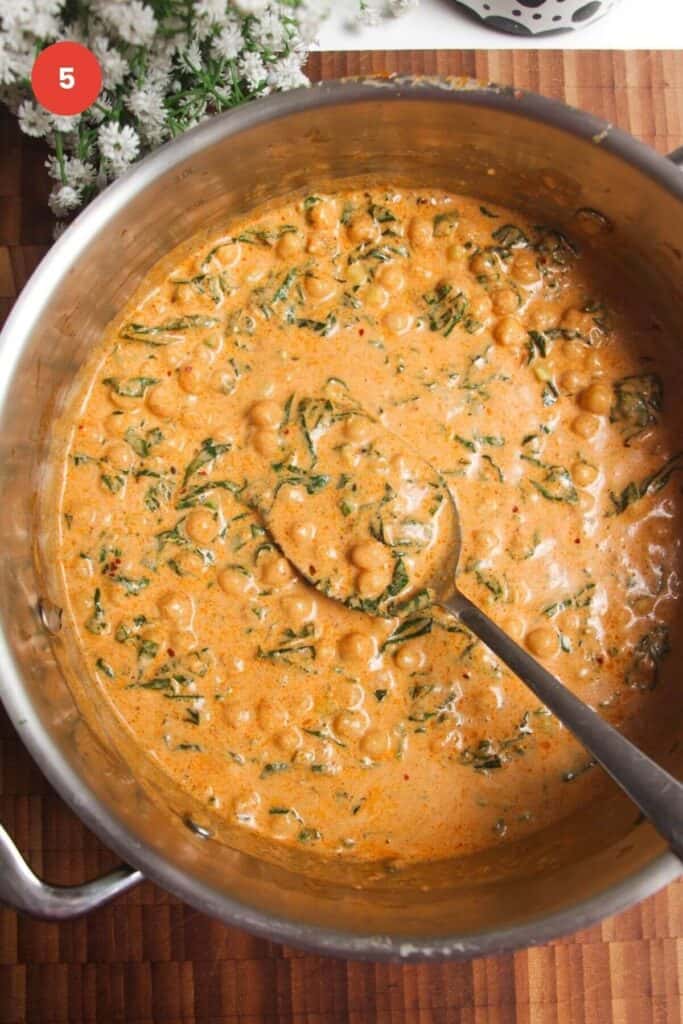 Spinach stirred through chickpeas in a large pan.